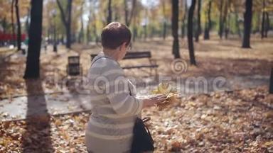 现在`是秋天的时候。 秋天公园的一位老妇人从地板上收集落叶。